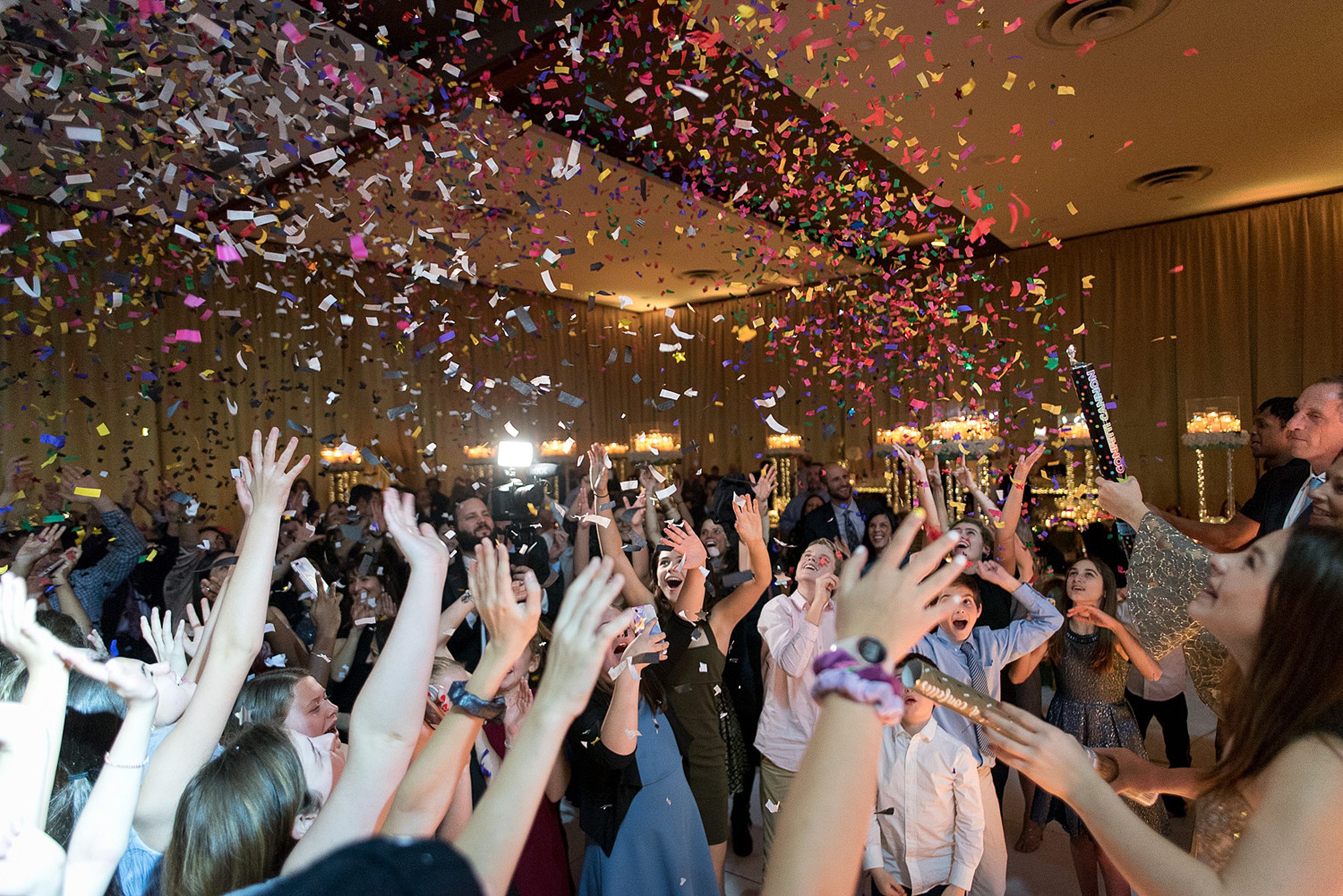Teenagers shoot off confetti cannons on the dance floor at a party with a Bar and Bat Mitzvah photographer