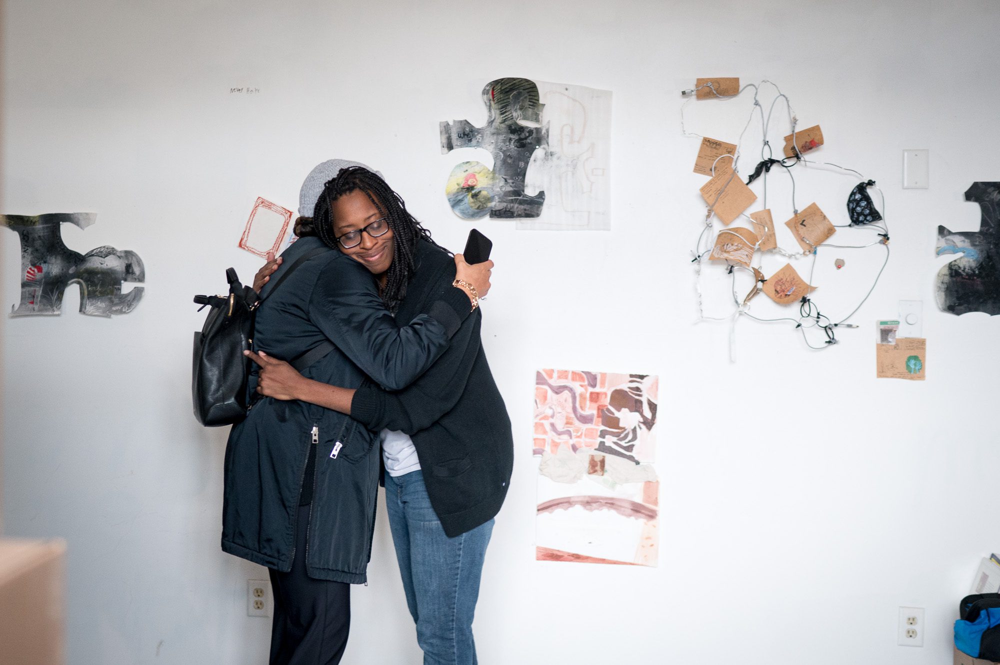 Two women hugging with artwork on the wall behind them