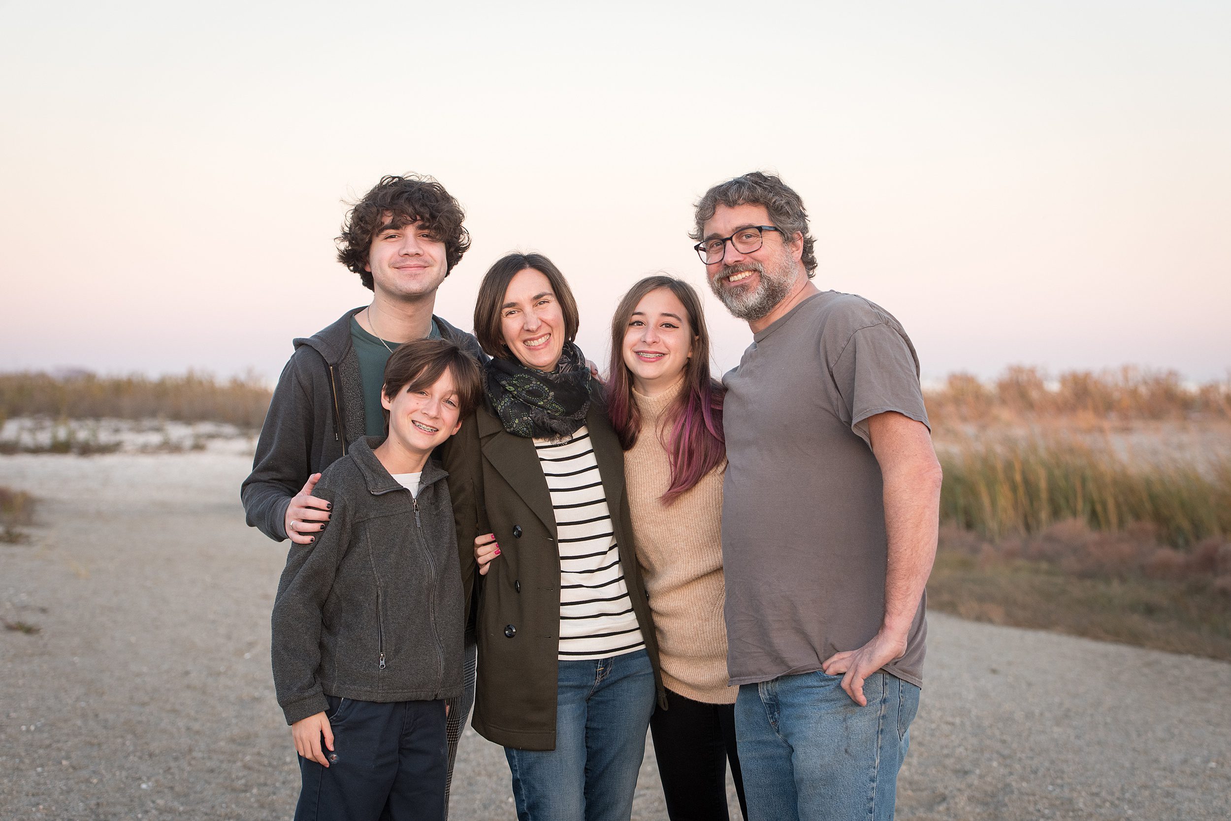 A family of five stands together hugging onto each other while smiling on the best connecticut beaches for families