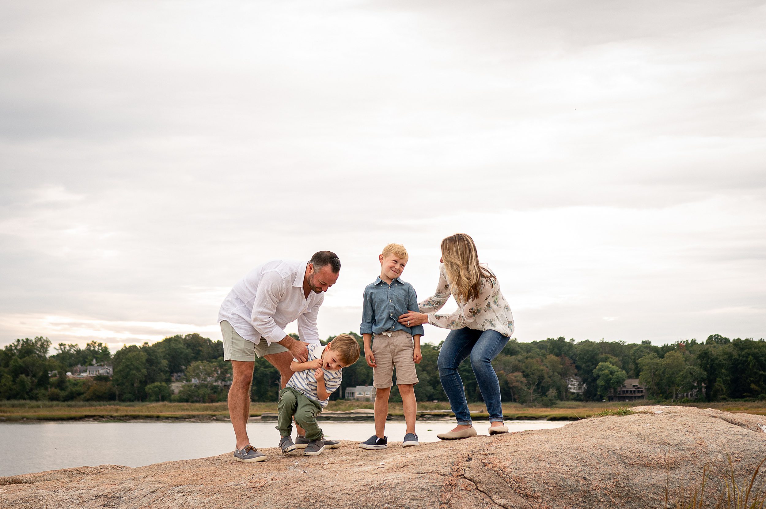 A mom and dad stand on a beach rock tickling their two young sons after they went to a preschool in Madison CT