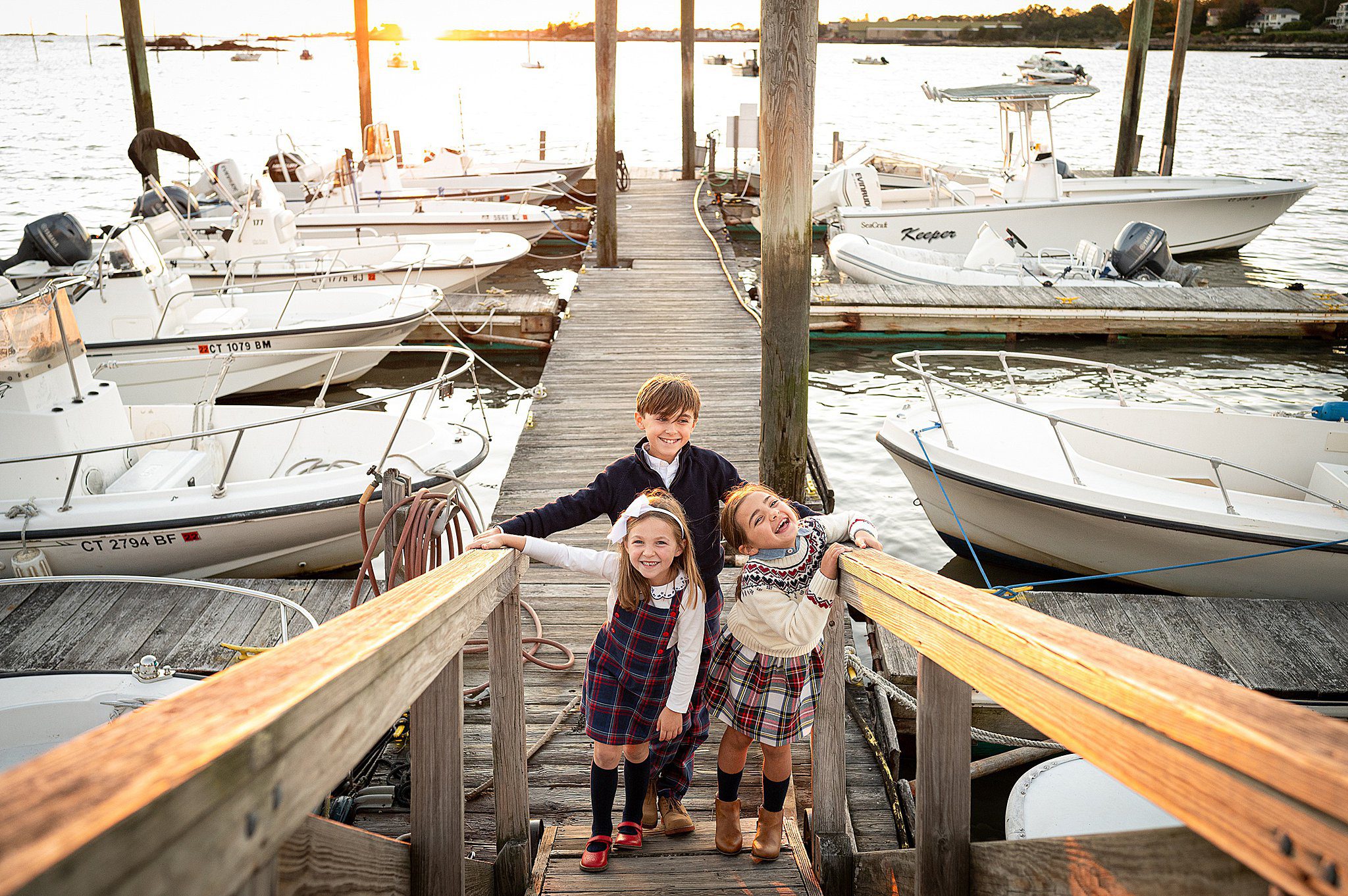 Three siblings laugh and play while walking up a boat ramp dock at sunset