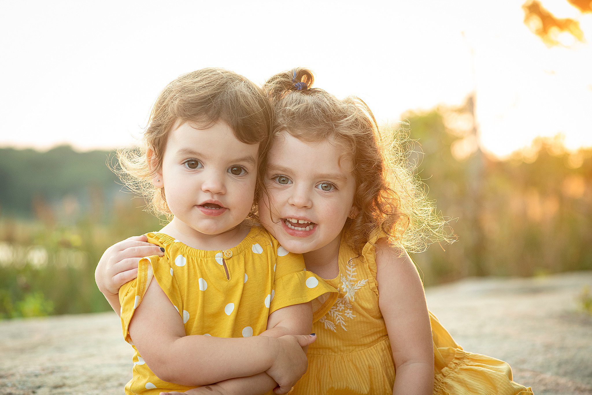 Two young toddler girls in yellow dresses sit in a park path at sunset before their birthday parties in connecticut