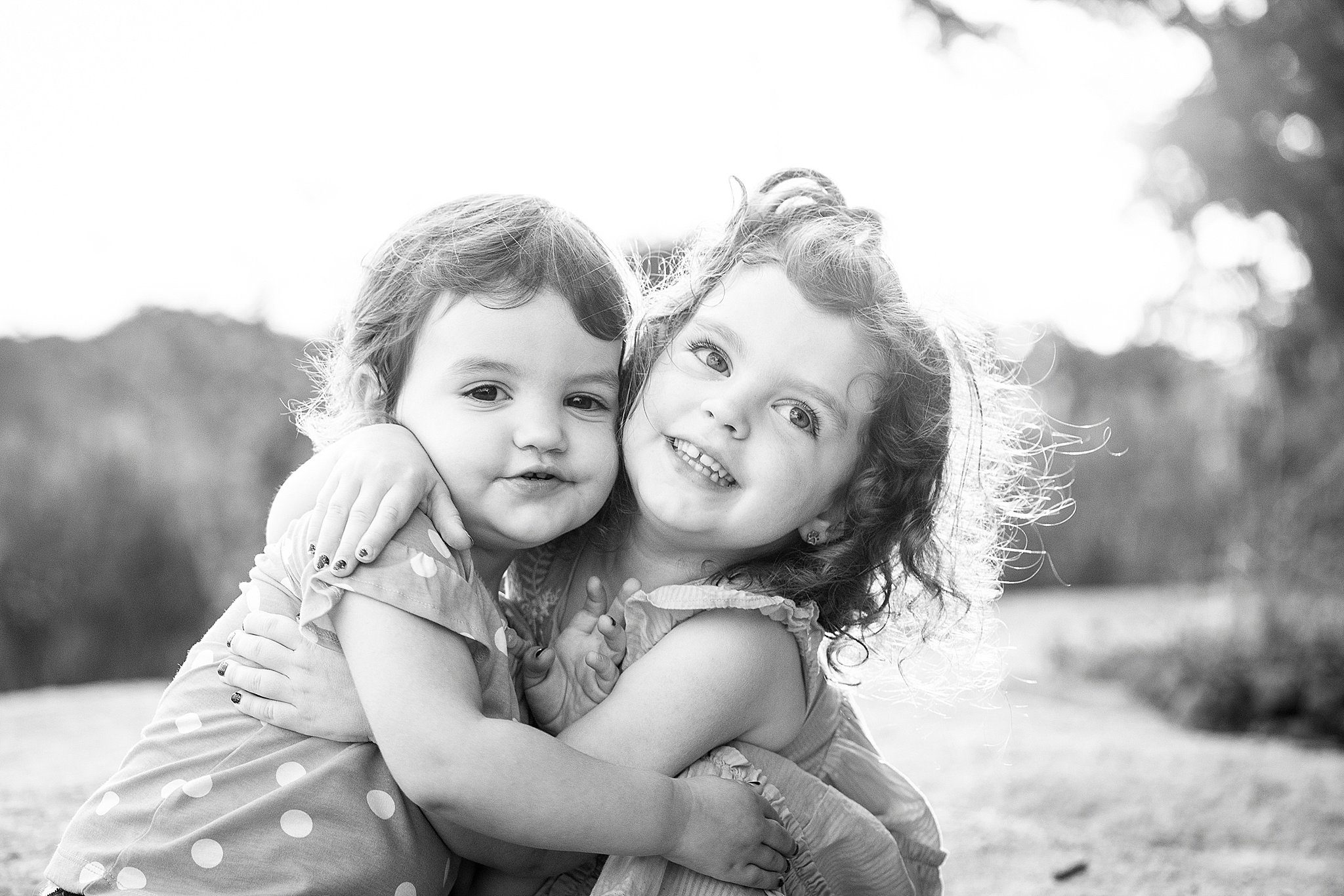 Two toddler sisters hug while sitting in a park before their birthday parties in connecticut