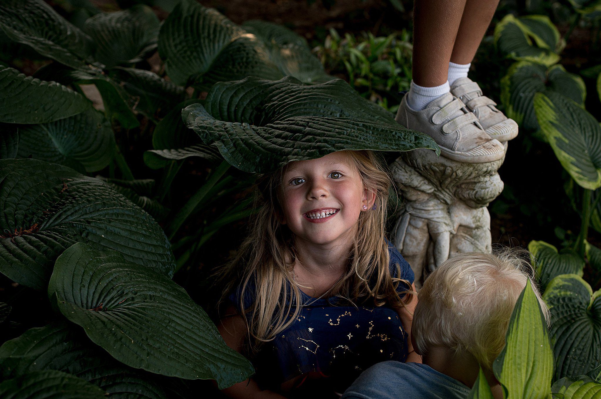 A young girl plays in a garden with her two siblings under a large leaf after daycare guildrod ct