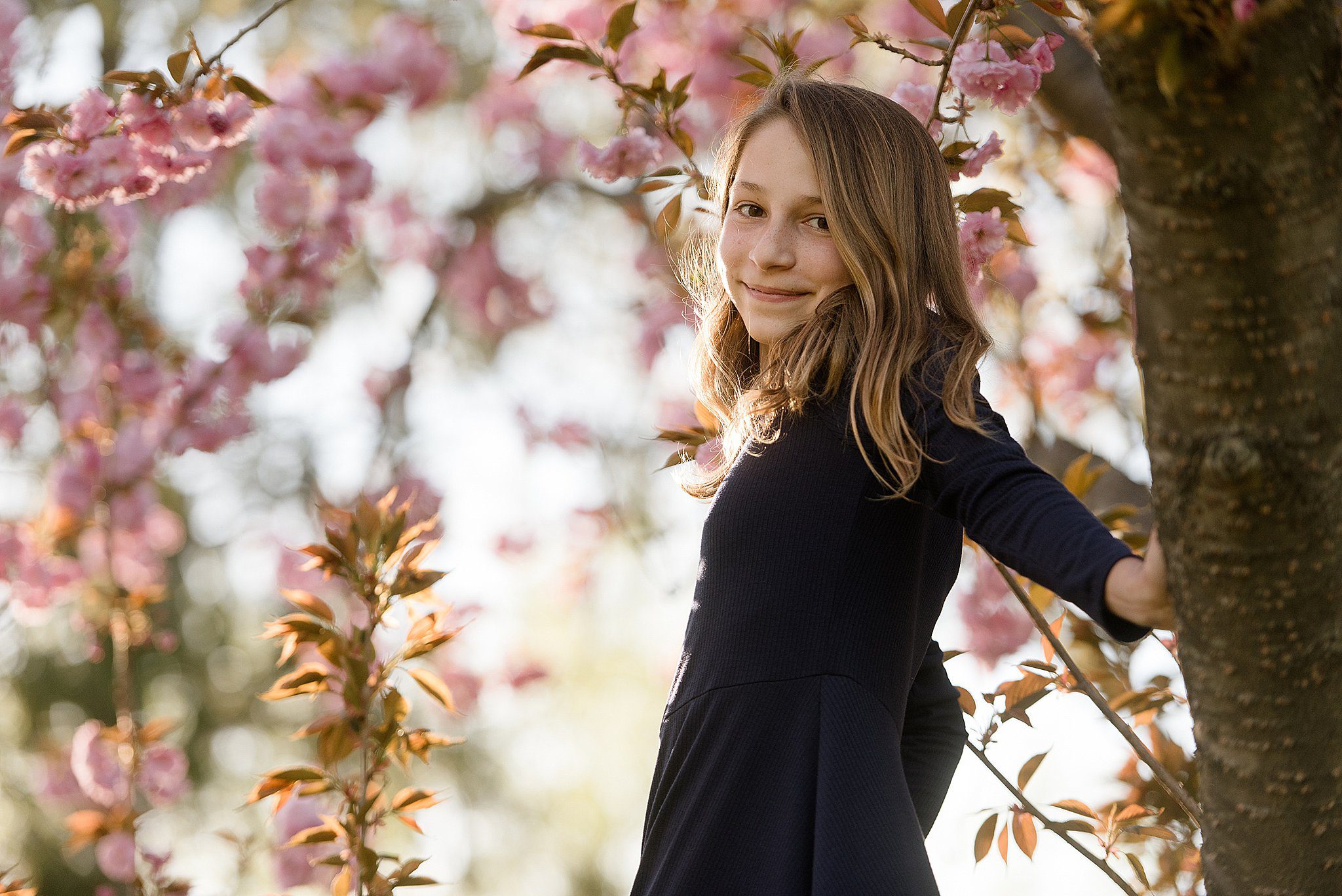A young girl in a blue dress stands in a flowering tree after meeting with nannies in connecticut