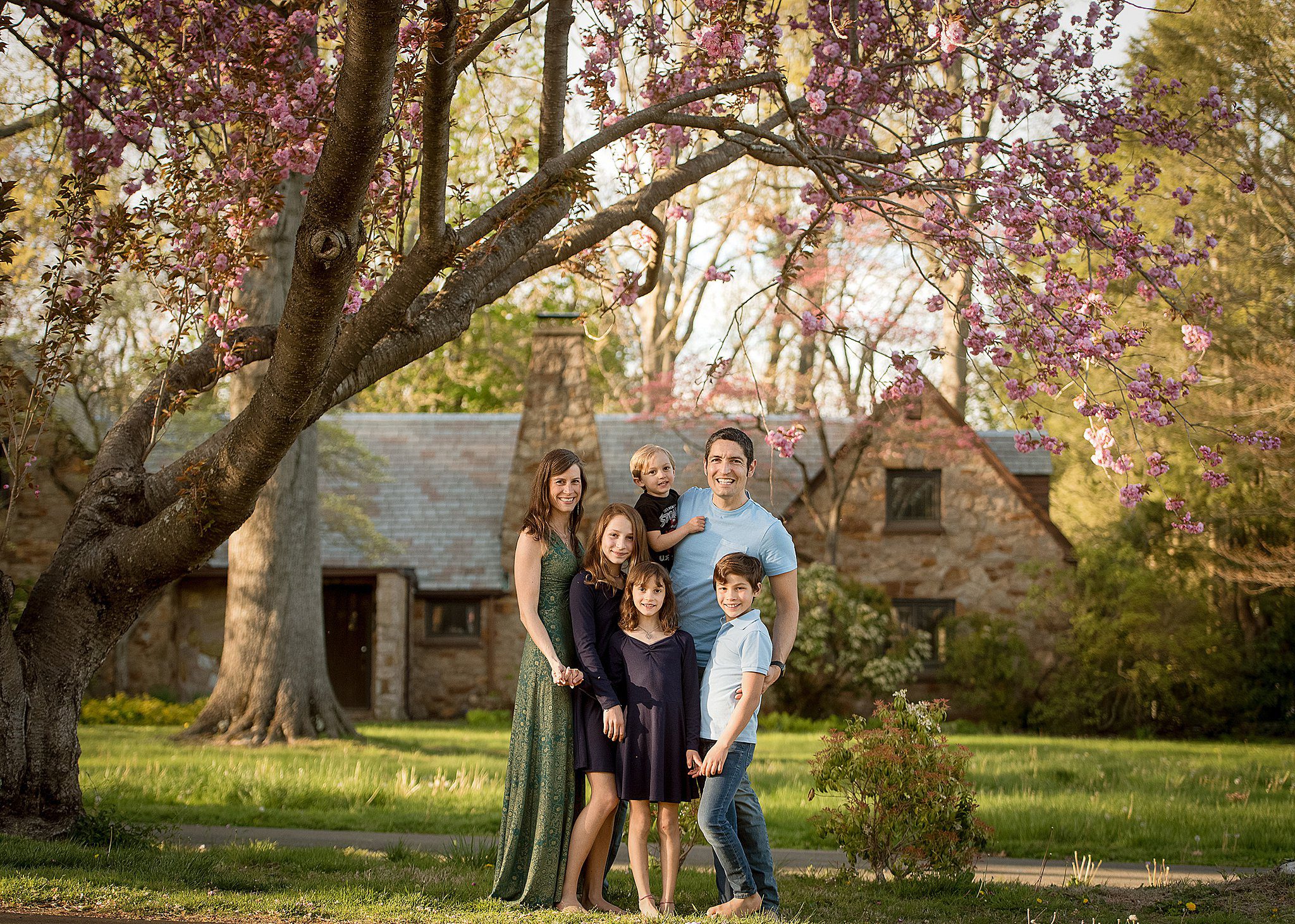 A family of 6 stand in their yard under a pink blooming tree after meeting nannies in connecticut