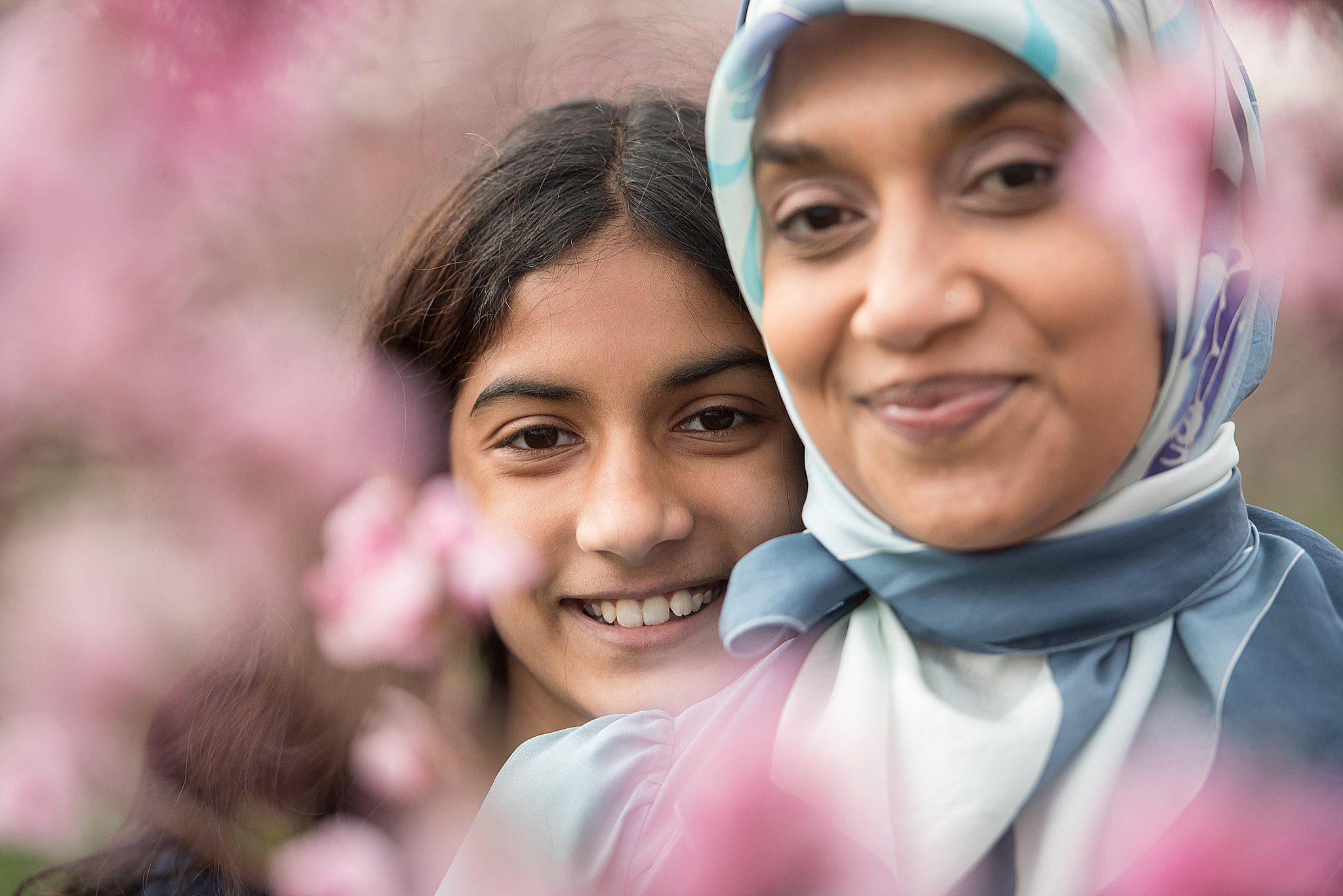 A mother in a blue hijab stands among pink flowers with her daughter behind her during things to do in guilford ct