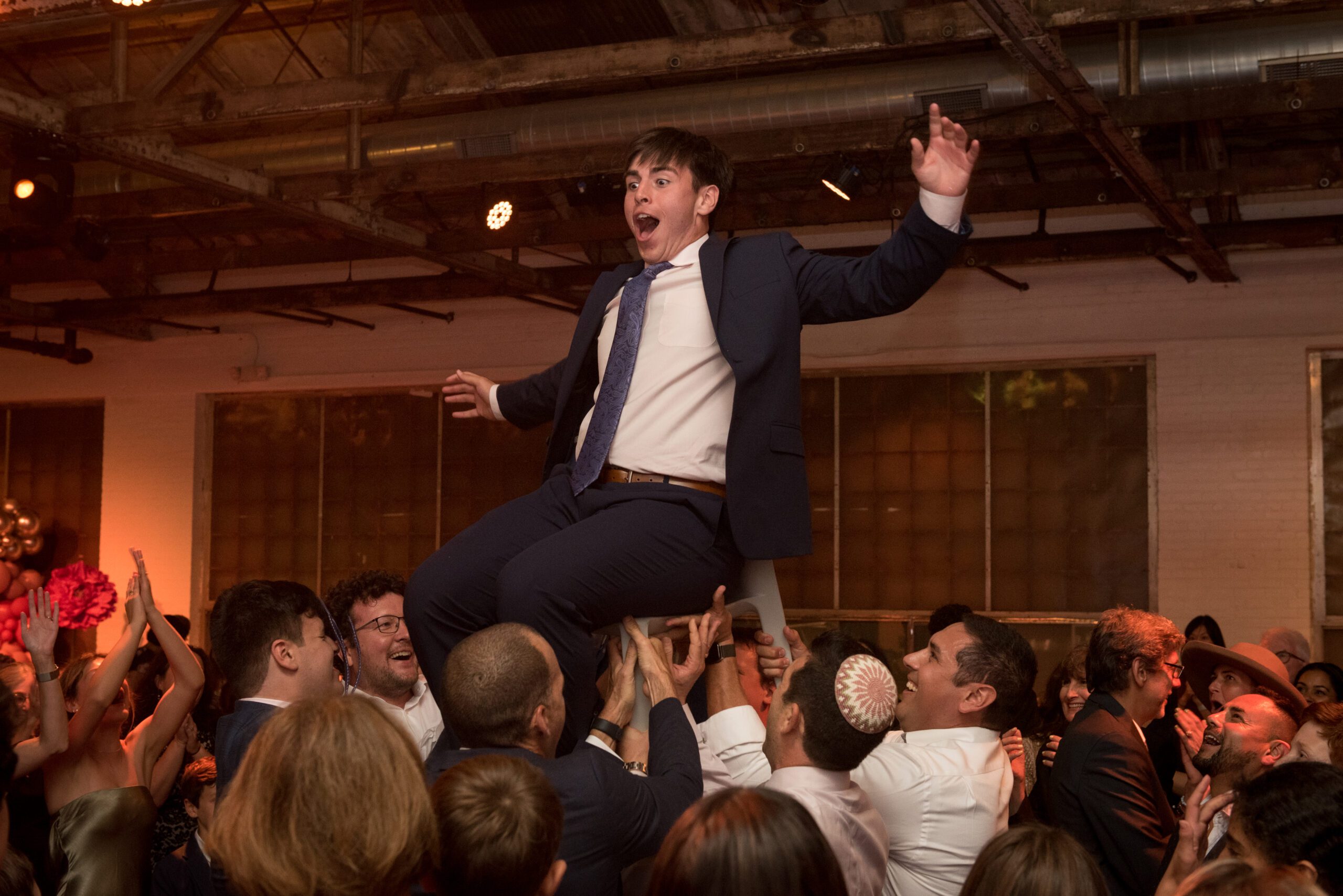A boy up in the hora chair at a bar mitzvah event