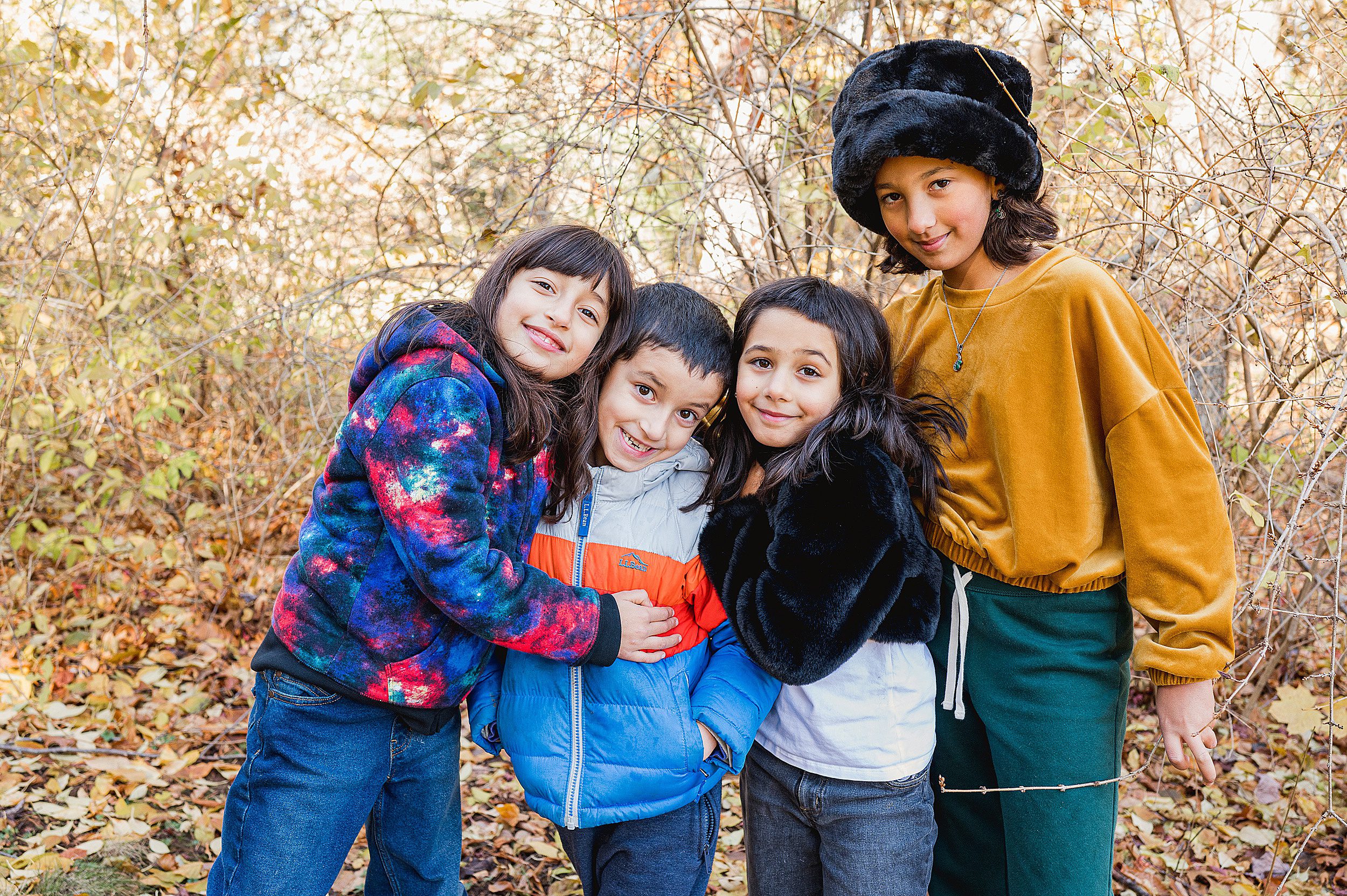 Three sisters and their brother all all cuddle close while standing in a forest in fall after meeting pediatrician madison ct