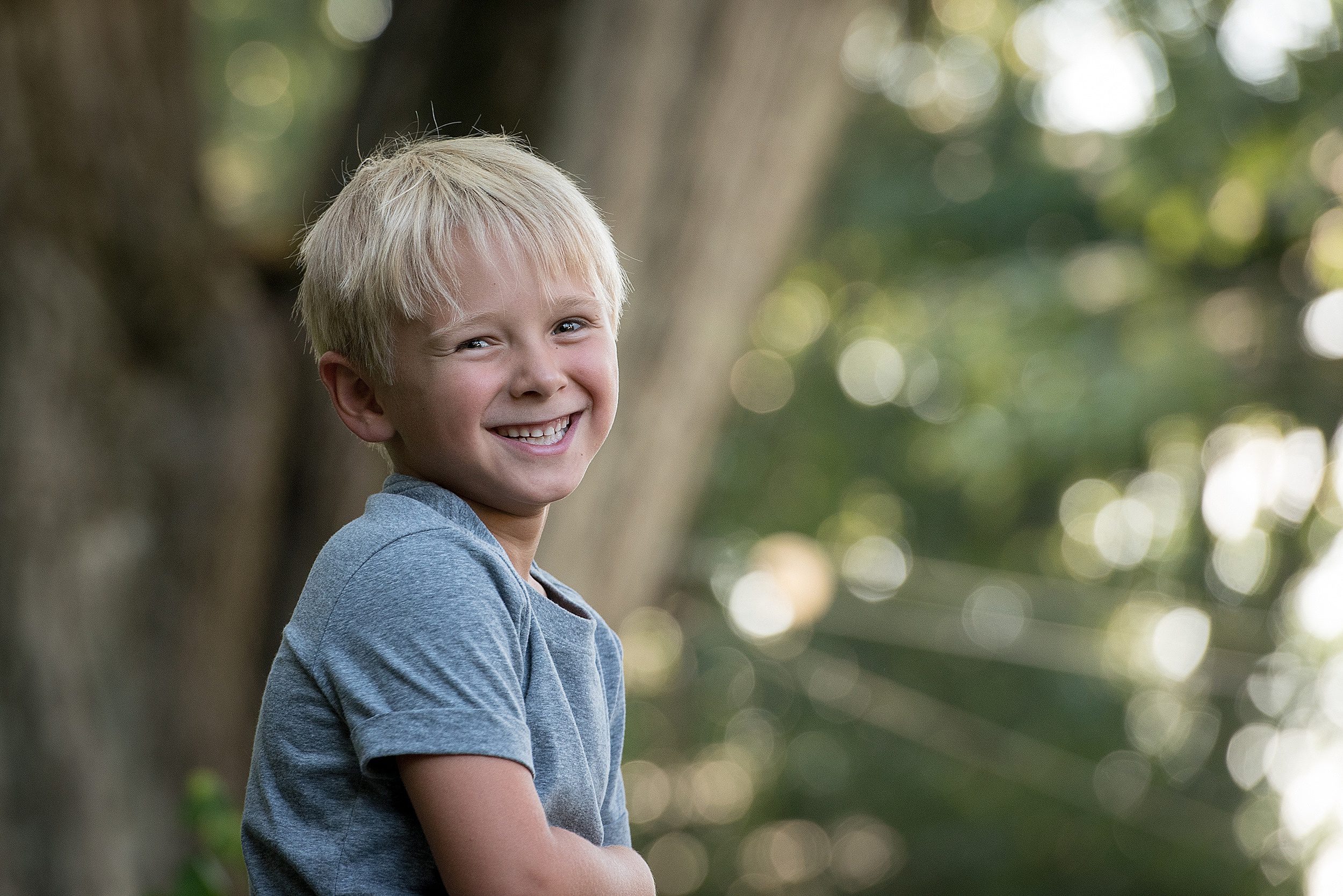 A young boy smiles in a grey shirt in a garden