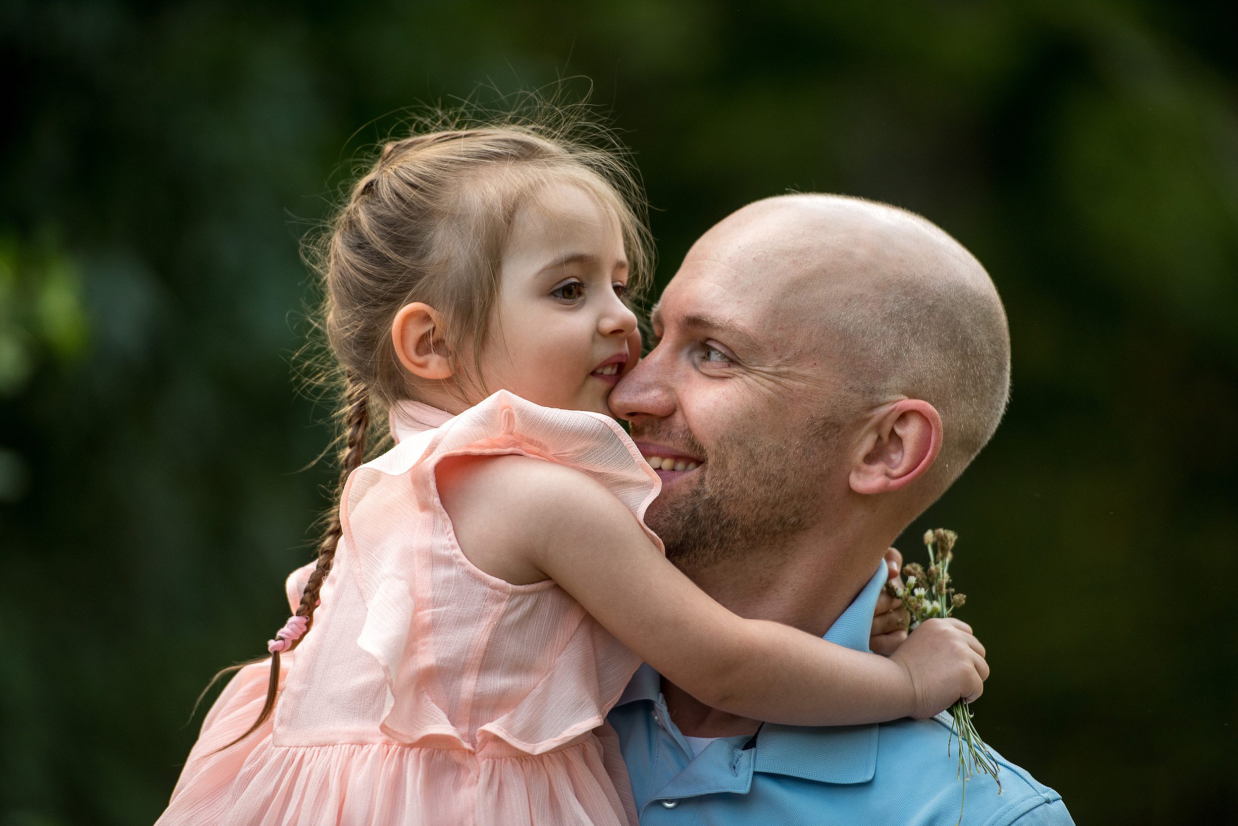A Happy father explores a park picking flowers with his toddler daughter in a pink dress