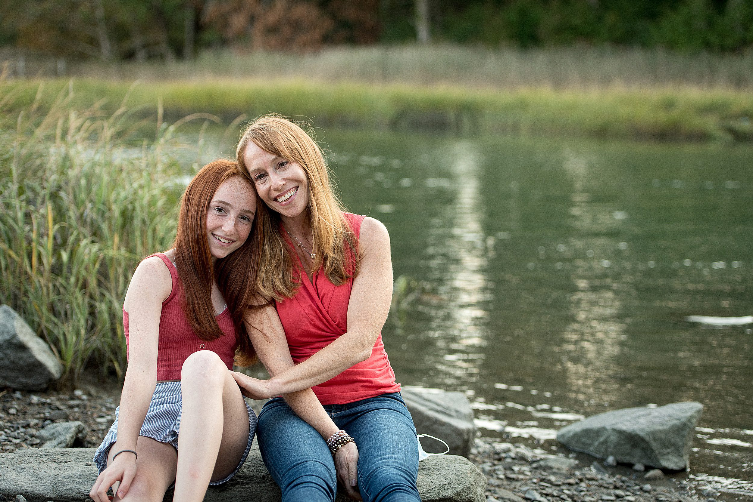 A mother in a pink shirt and jeans sits on a riverside rock with her teen daughter after some swim lessons guilford ct