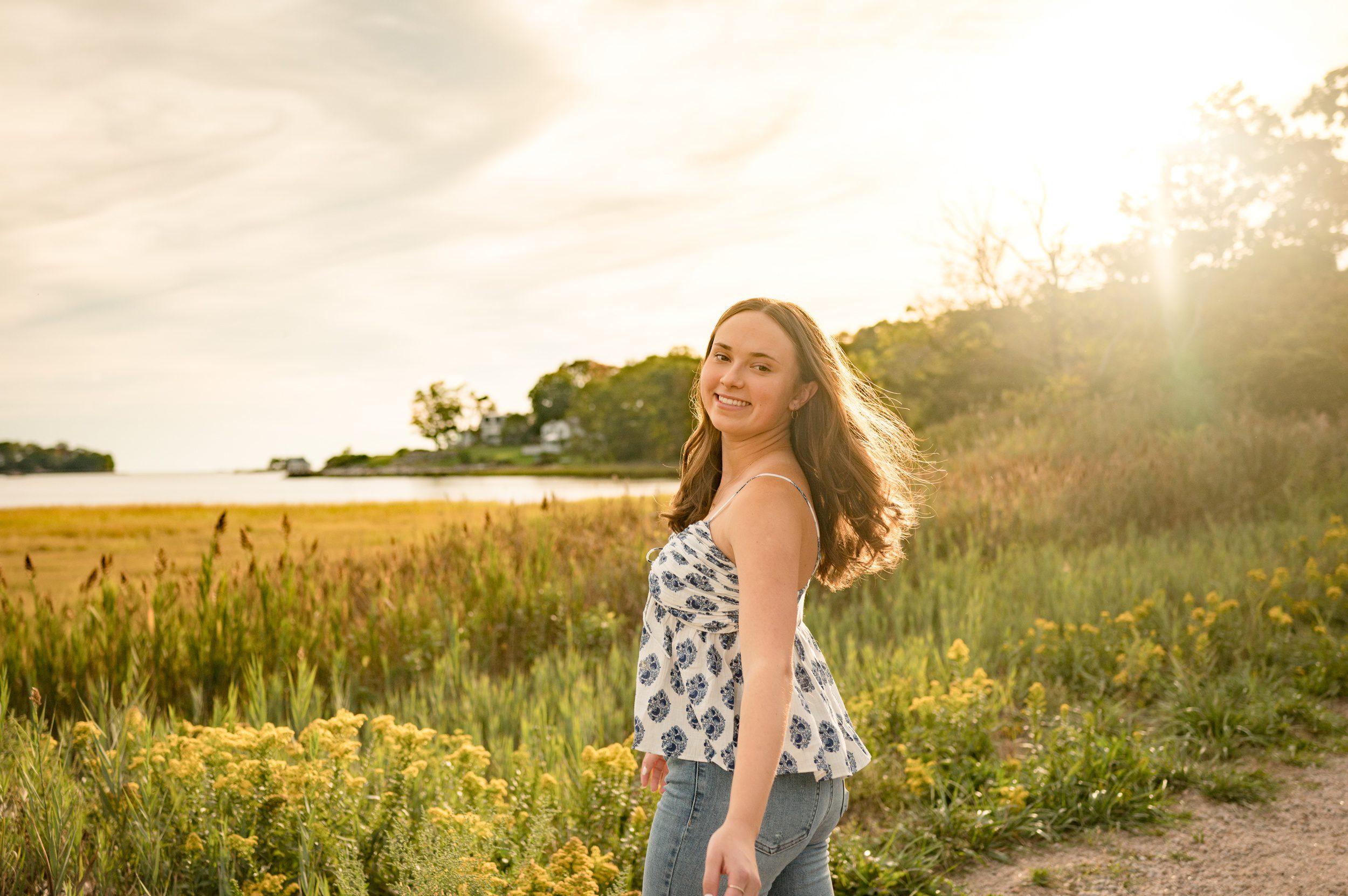 A happy high school senior walking on a waterfront trail smiling over her shoulder at sunset