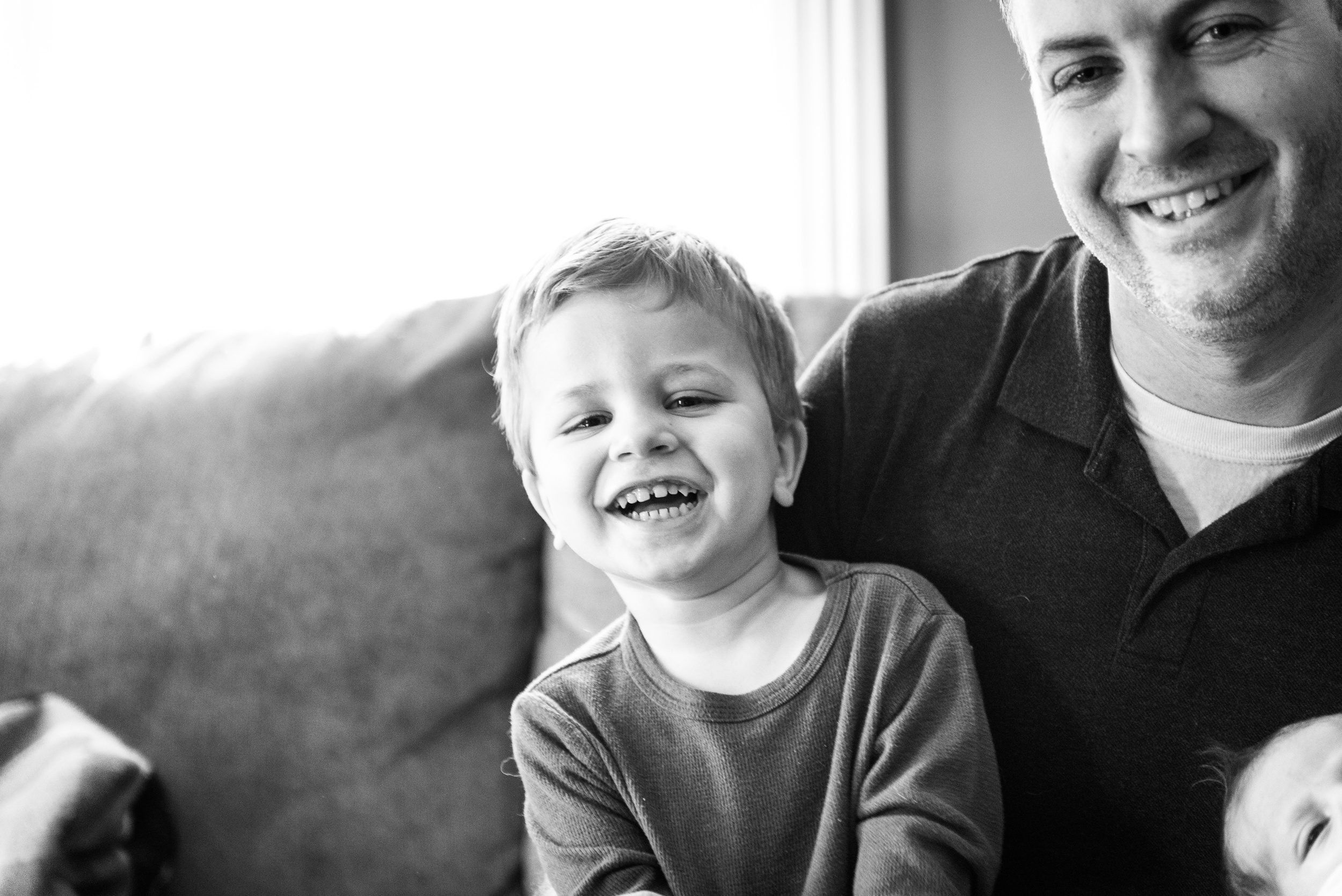 Happy toddler boy sits in dad's lap on a couch laughing