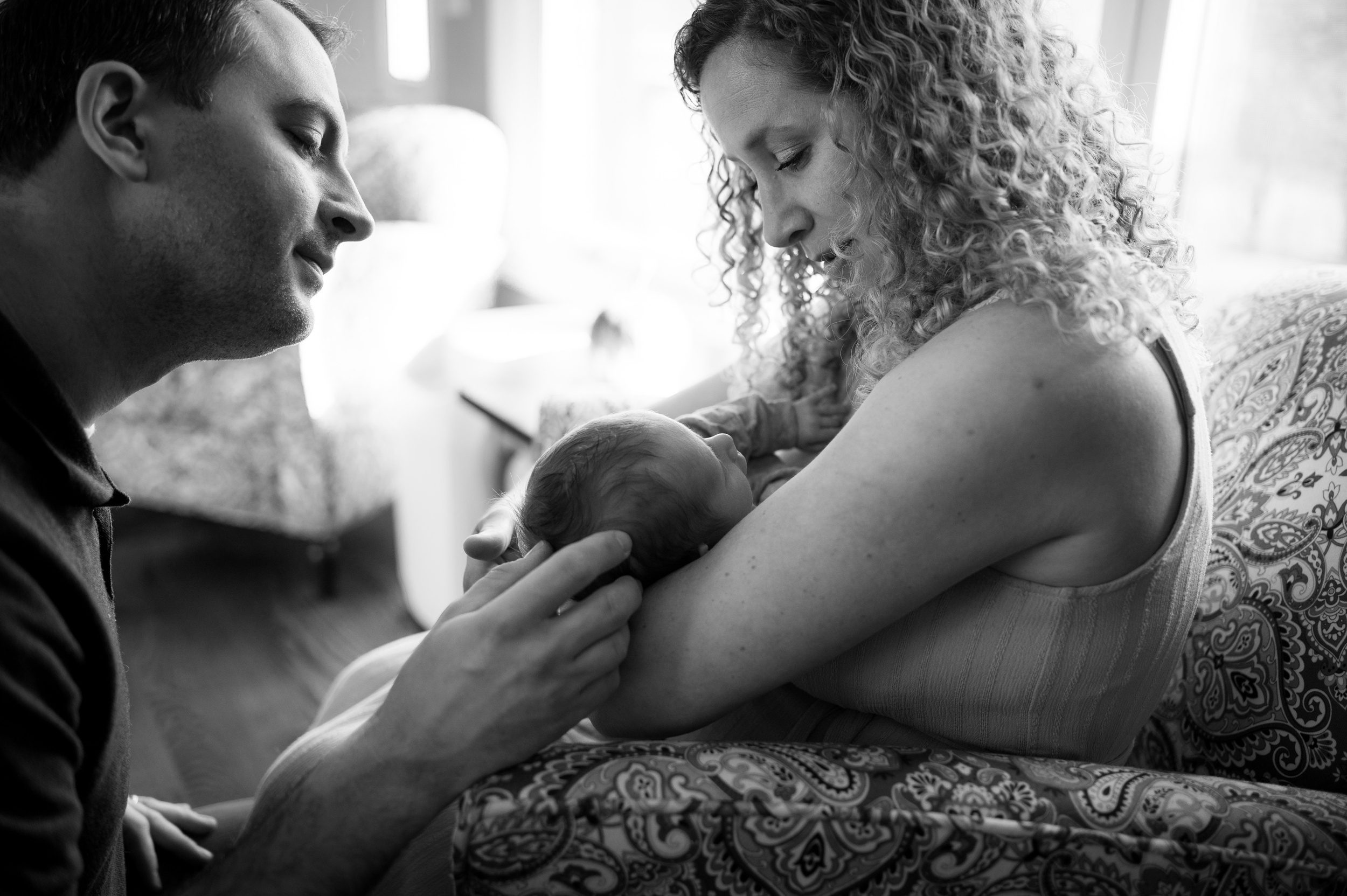 Happy new parents admire their sleeping newborn in mom's arms on a couch after some parenting classes in connecticut