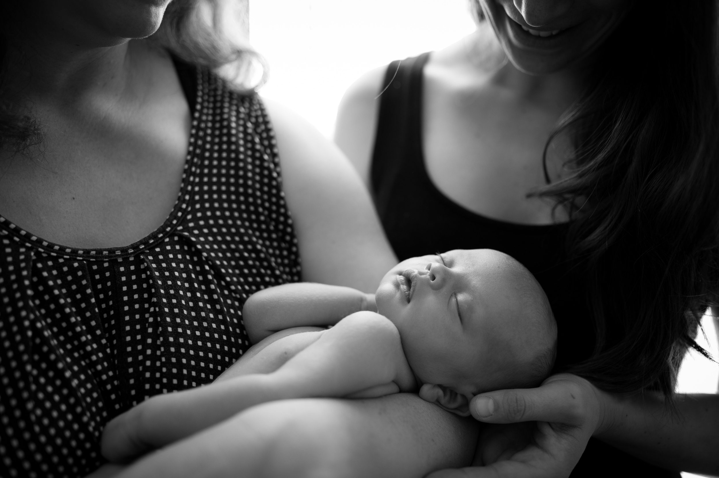 A newborn baby sleeps in mom's arms as teen older sister looks on