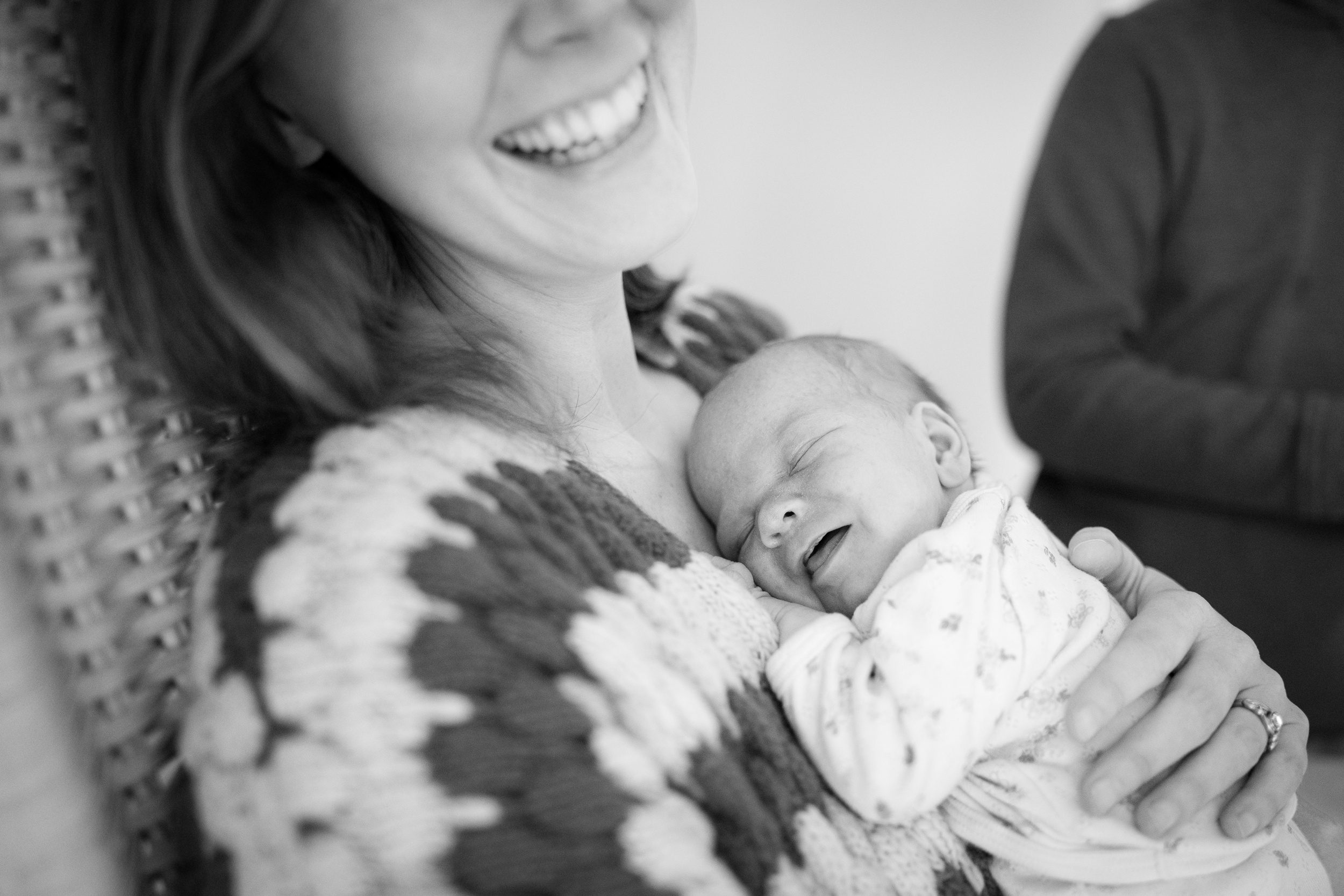 A newborn baby smiles while sleeping on mom's chest in a wicker chair after some pelvic floor physical therapy in CT