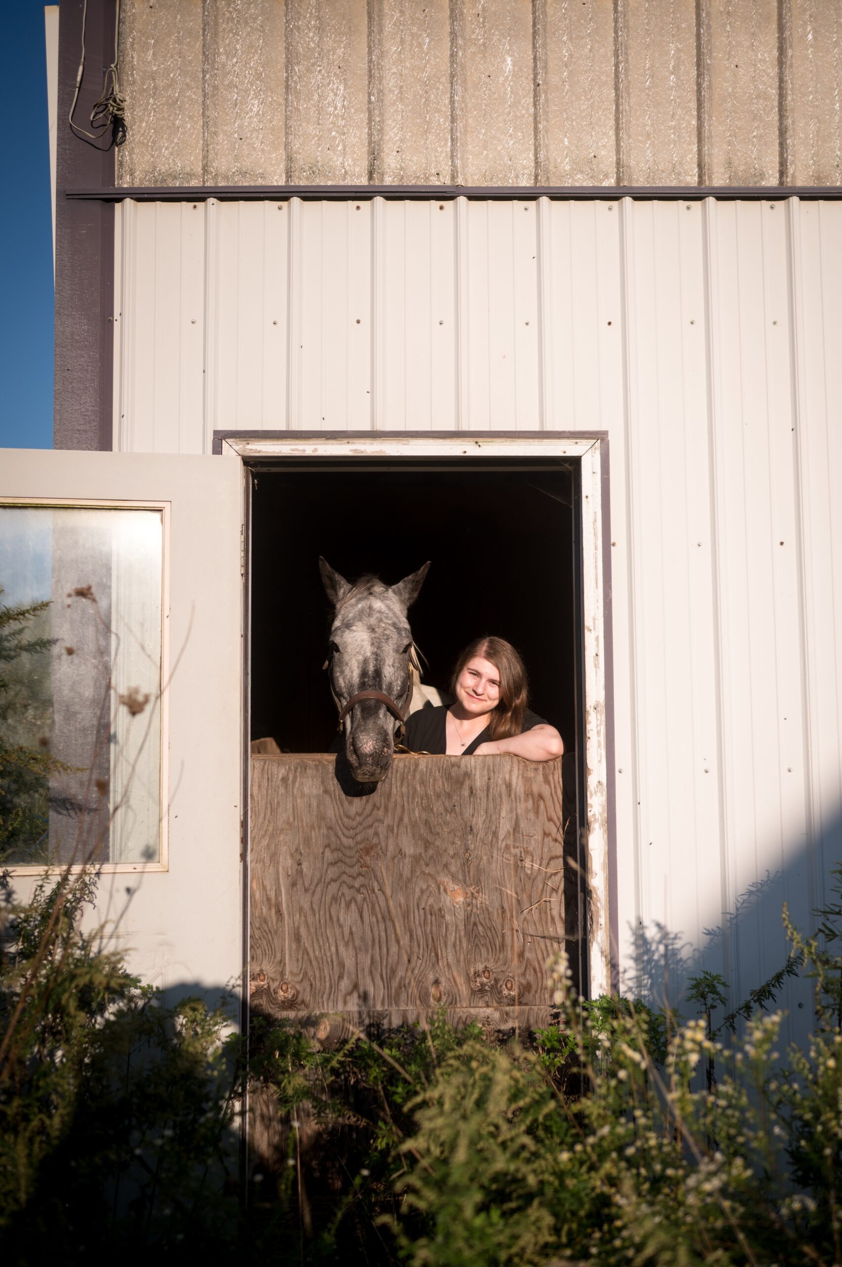 A sacred heart academy hamden senior stands in a stall with a horse