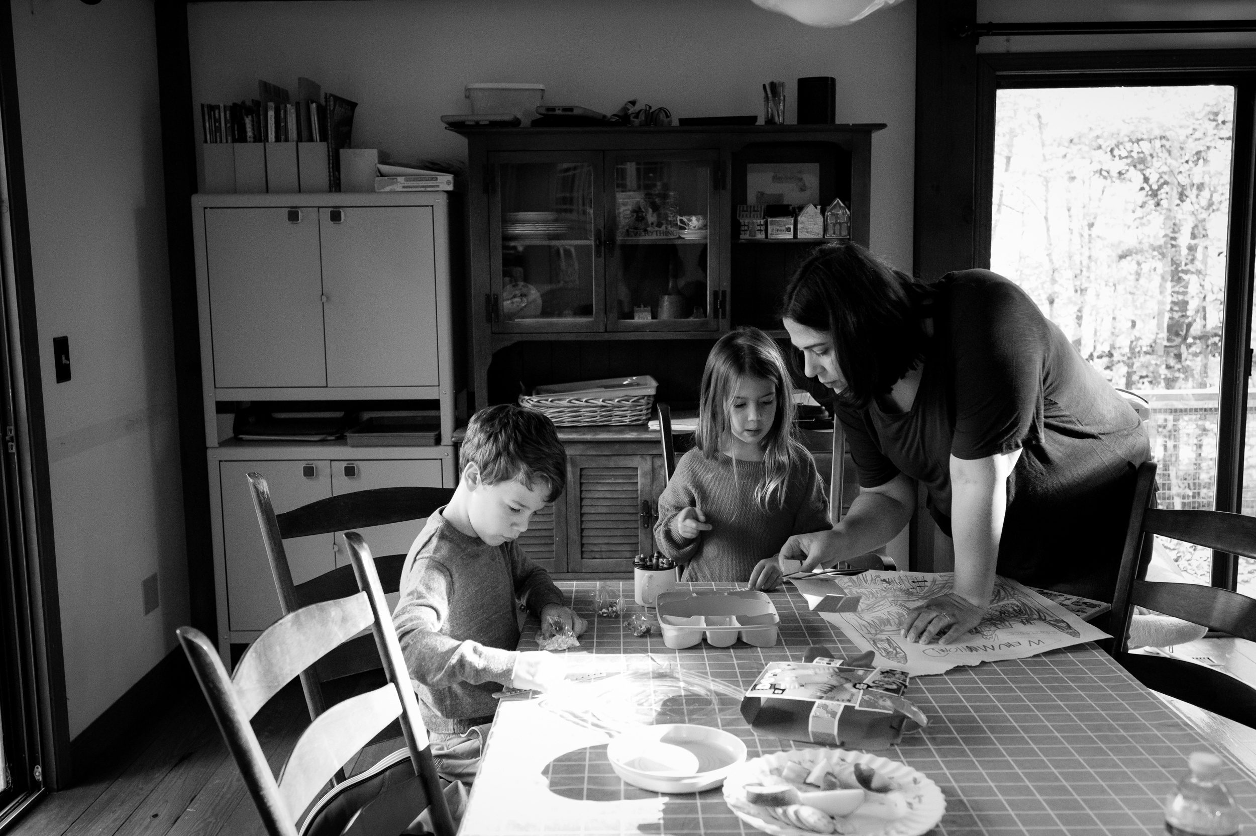 A mom helps her toddler son and daughter color at the kitchen table