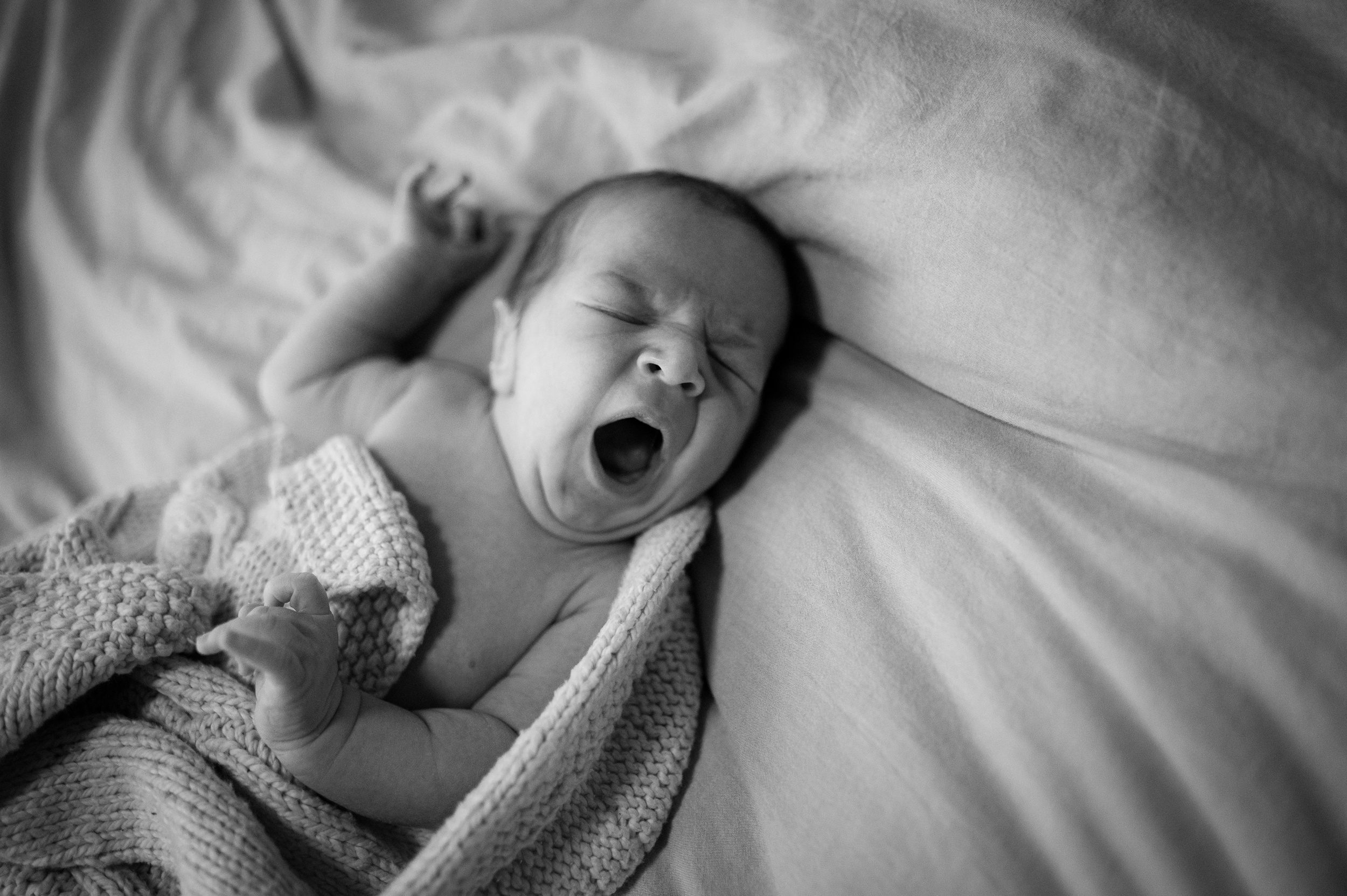 A newborn baby in a knit blanket yawns while sleeping on a bed before doing things to do in new haven with kids