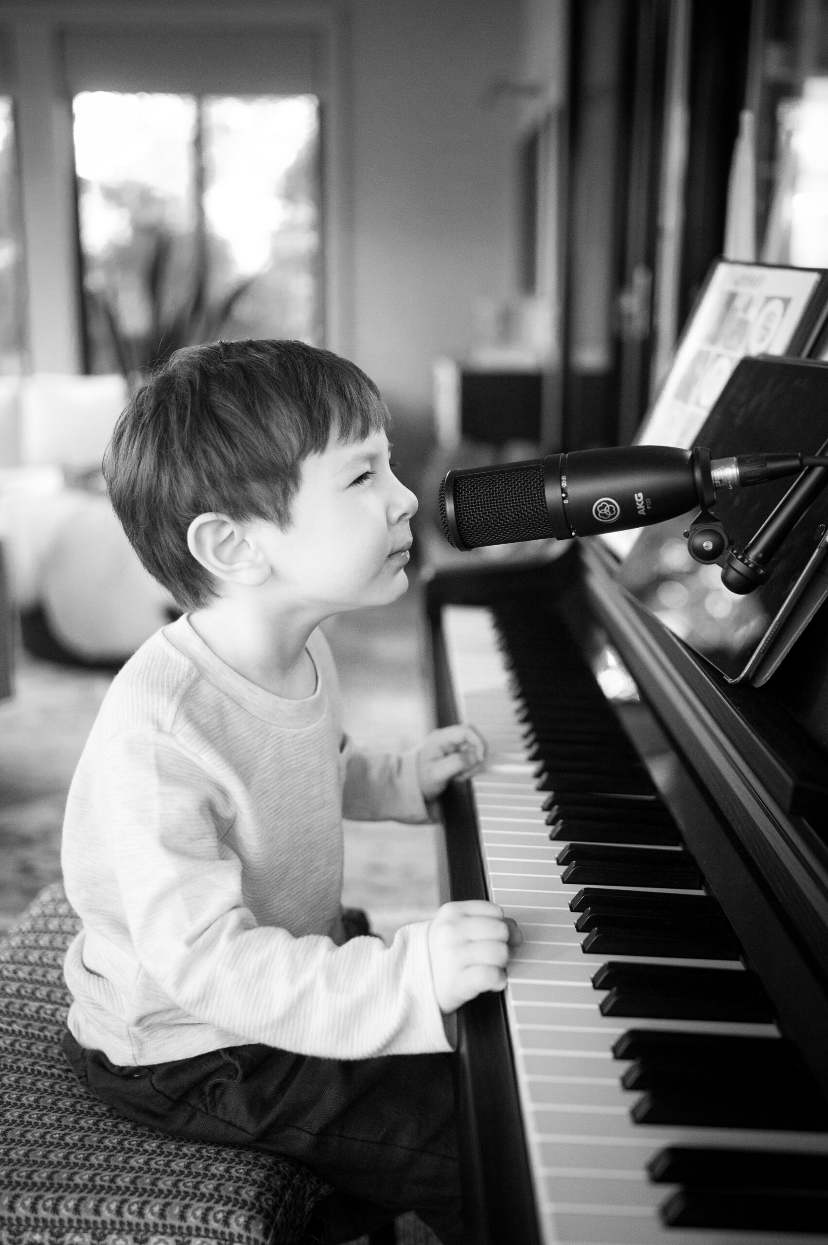A young boy sits at the piano singing into the microphone in a living room