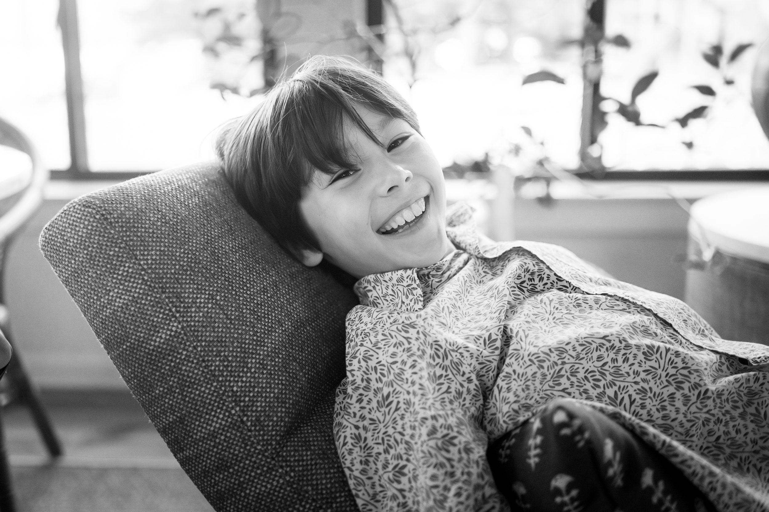 A happy boy in a print button down shirt laughs while leaning back in some kids furniture in ct
