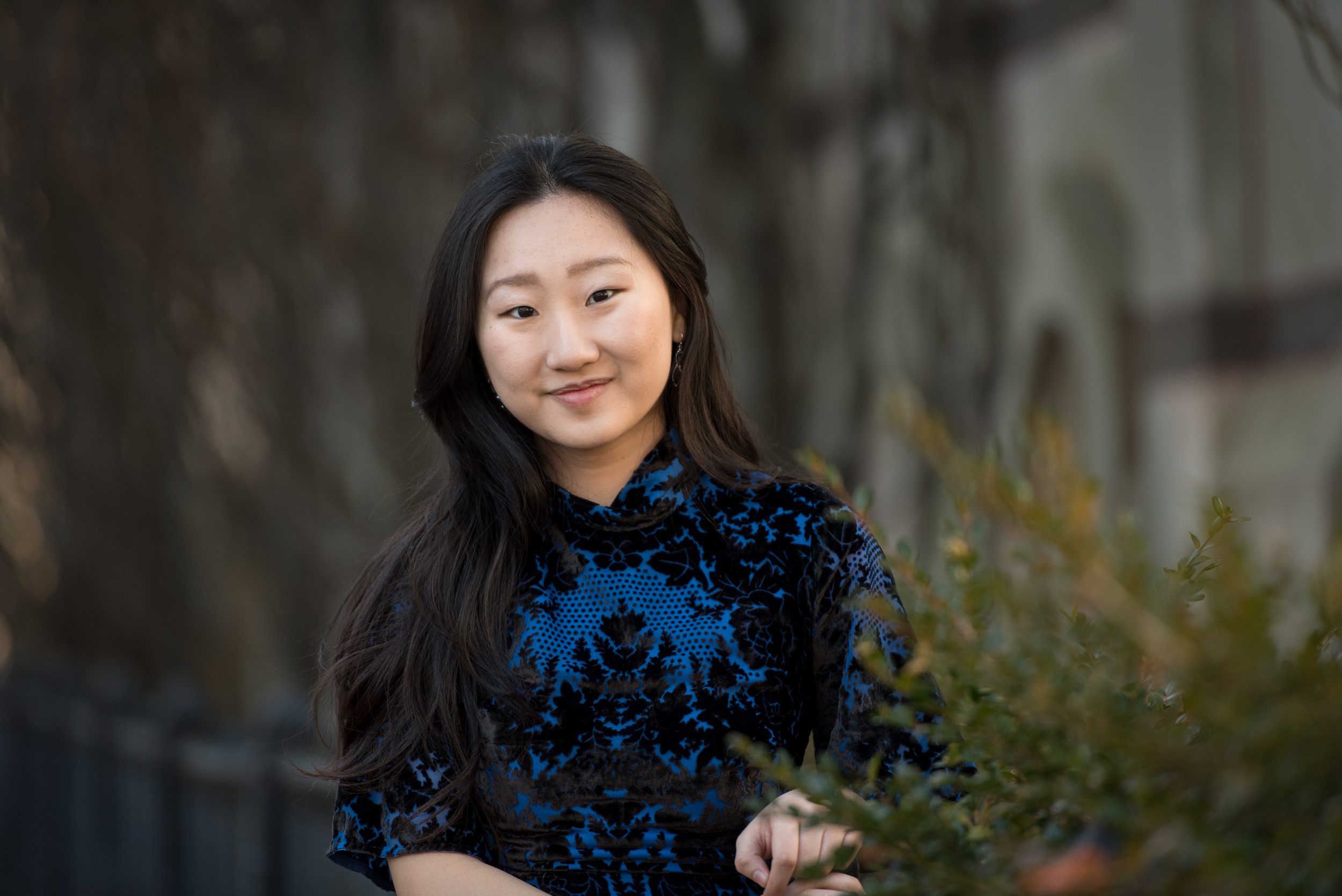 A high school senior in a blue dress leans on a fence in a garden smiling after meeting with the learning edge