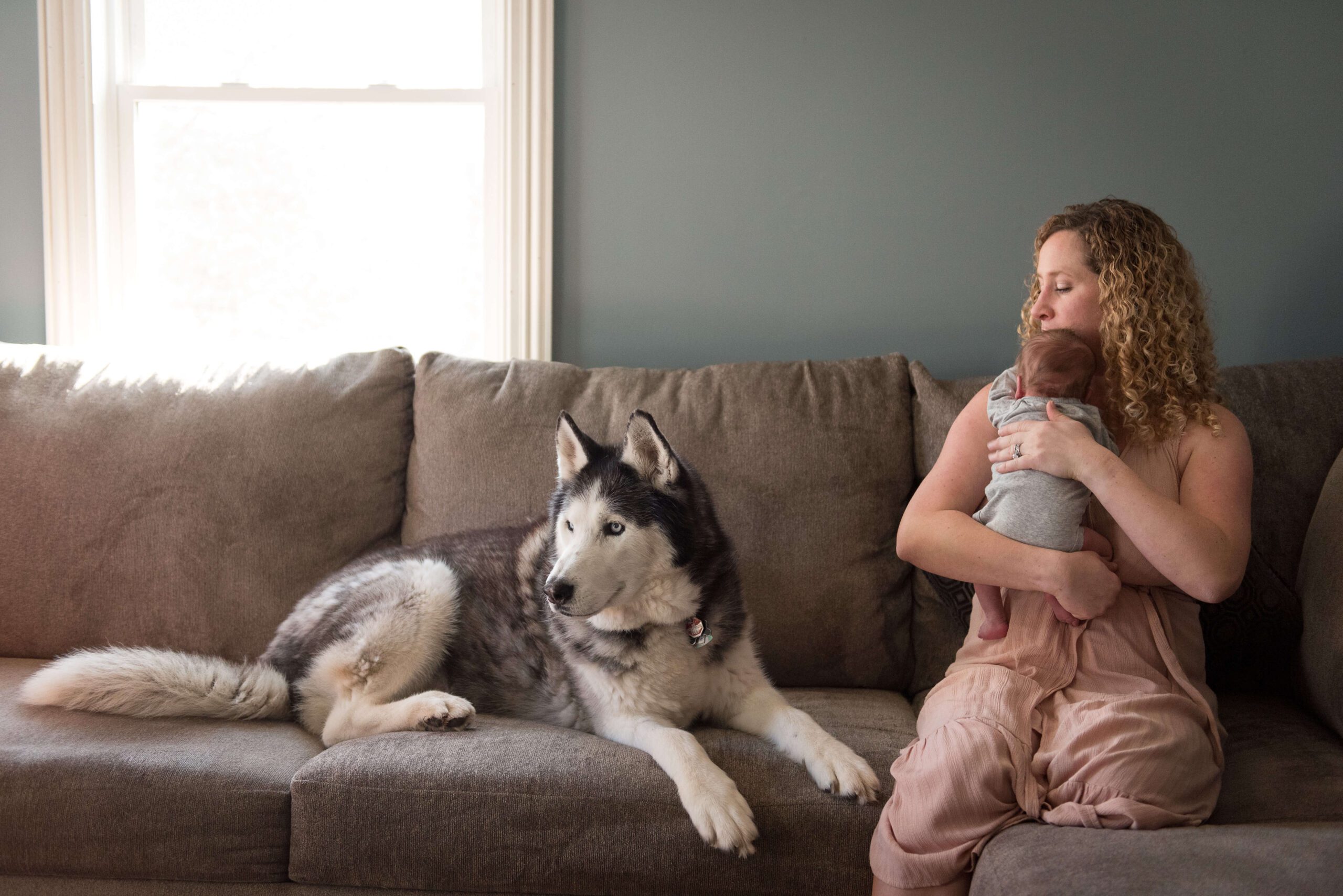 A mother cradles her newborn baby on a couch next to her large husky