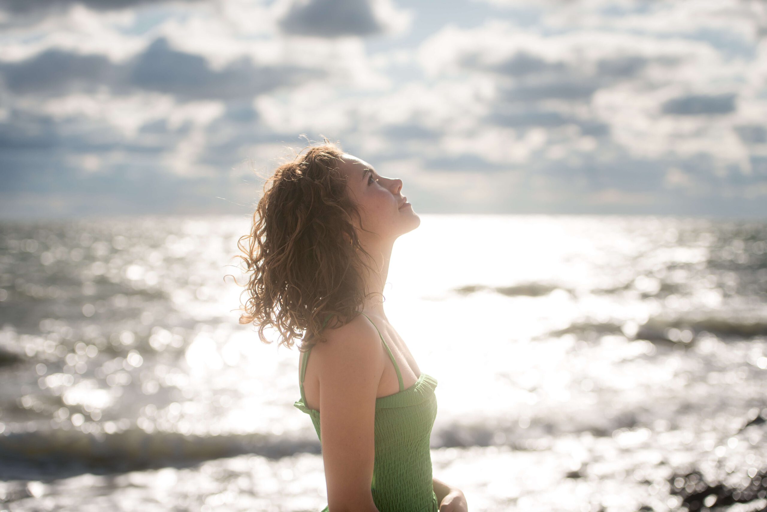 A high school senior stands by the ocean staring up in a green dress after finding great hair salons in new haven