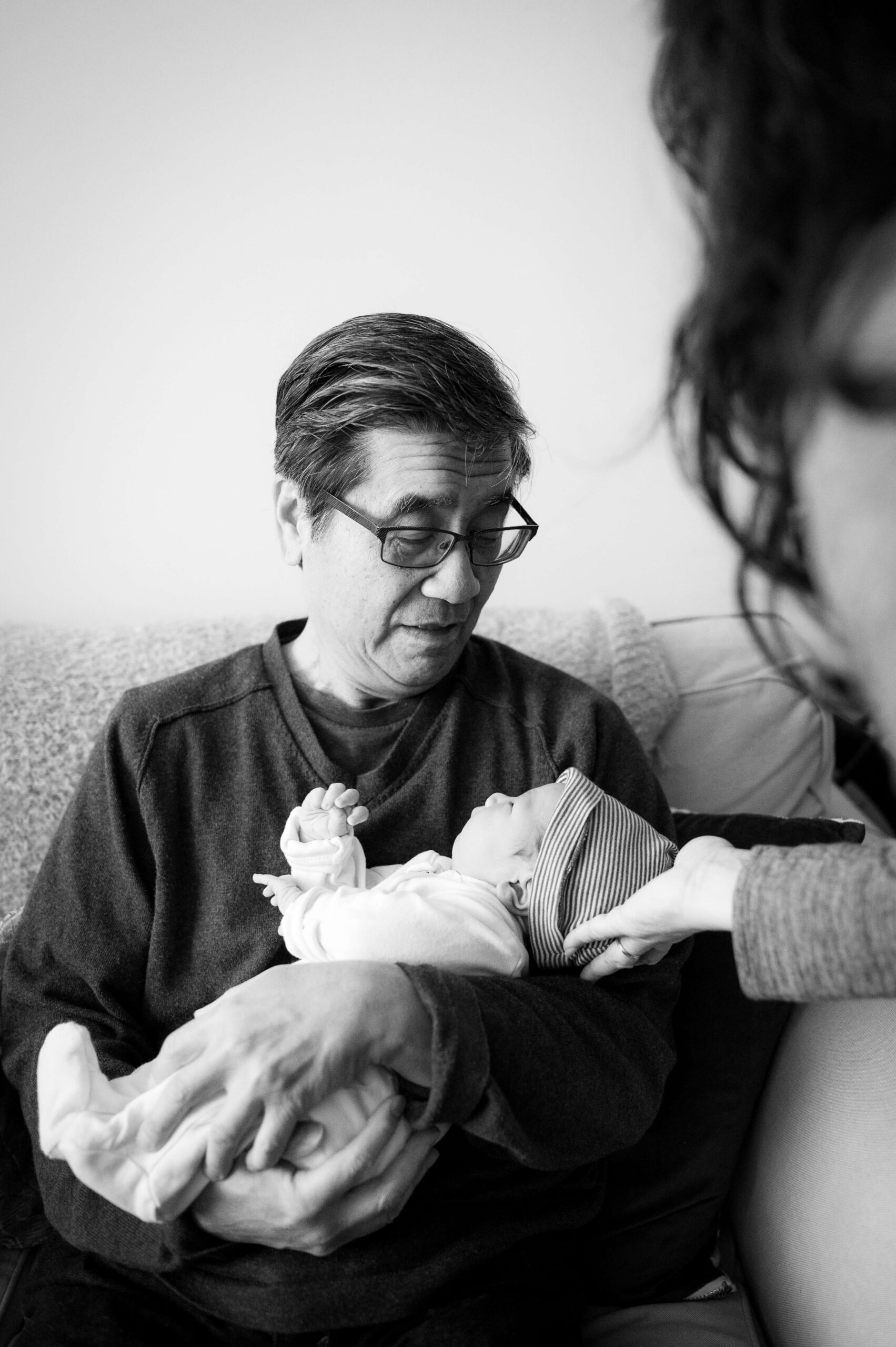 A grandfather cradles his newborn grandchild while sitting on a couch
