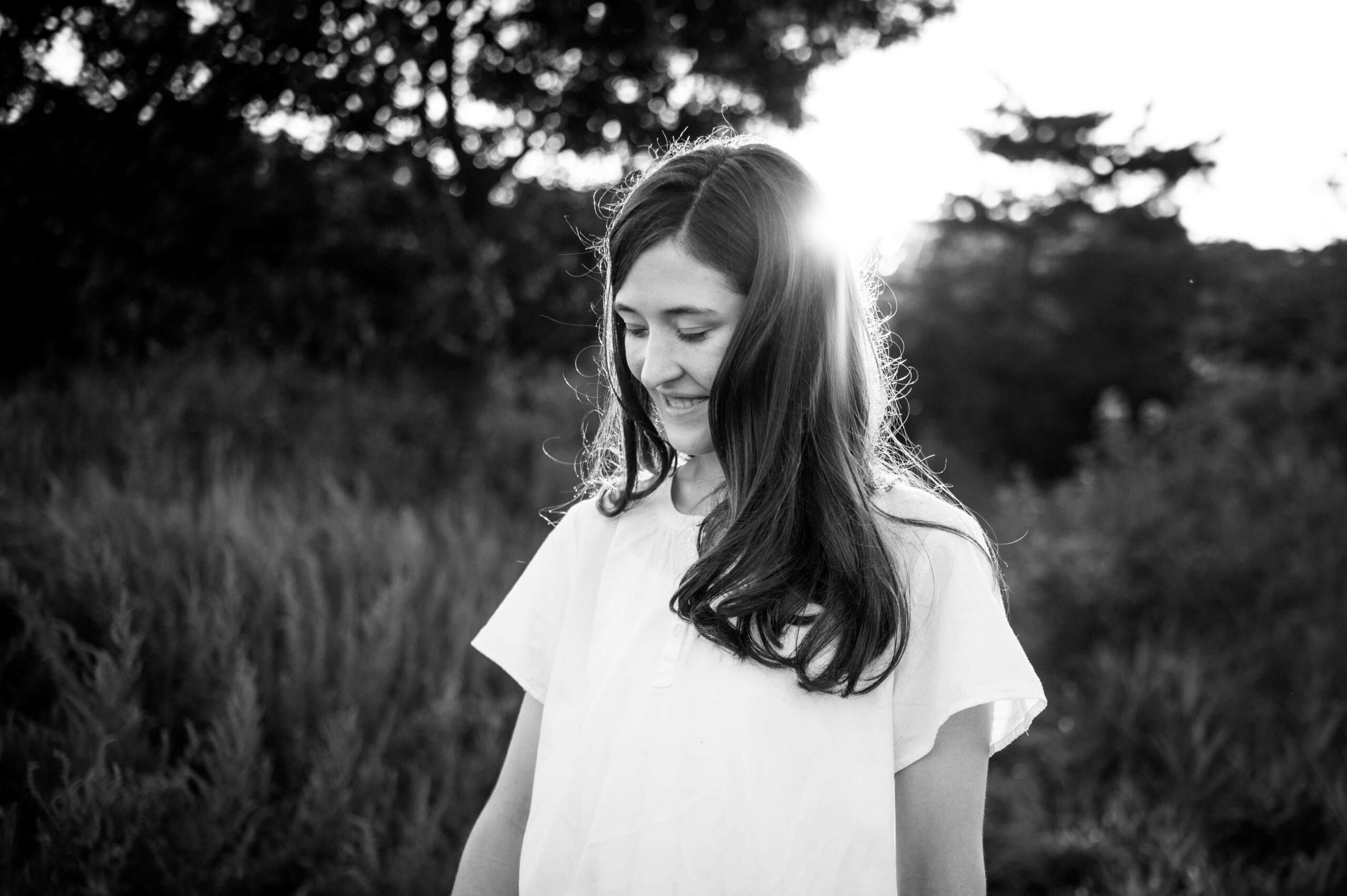 A high school senior in a white blouse walks in tall grass at sunset smiling after visiting boutiques in new haven