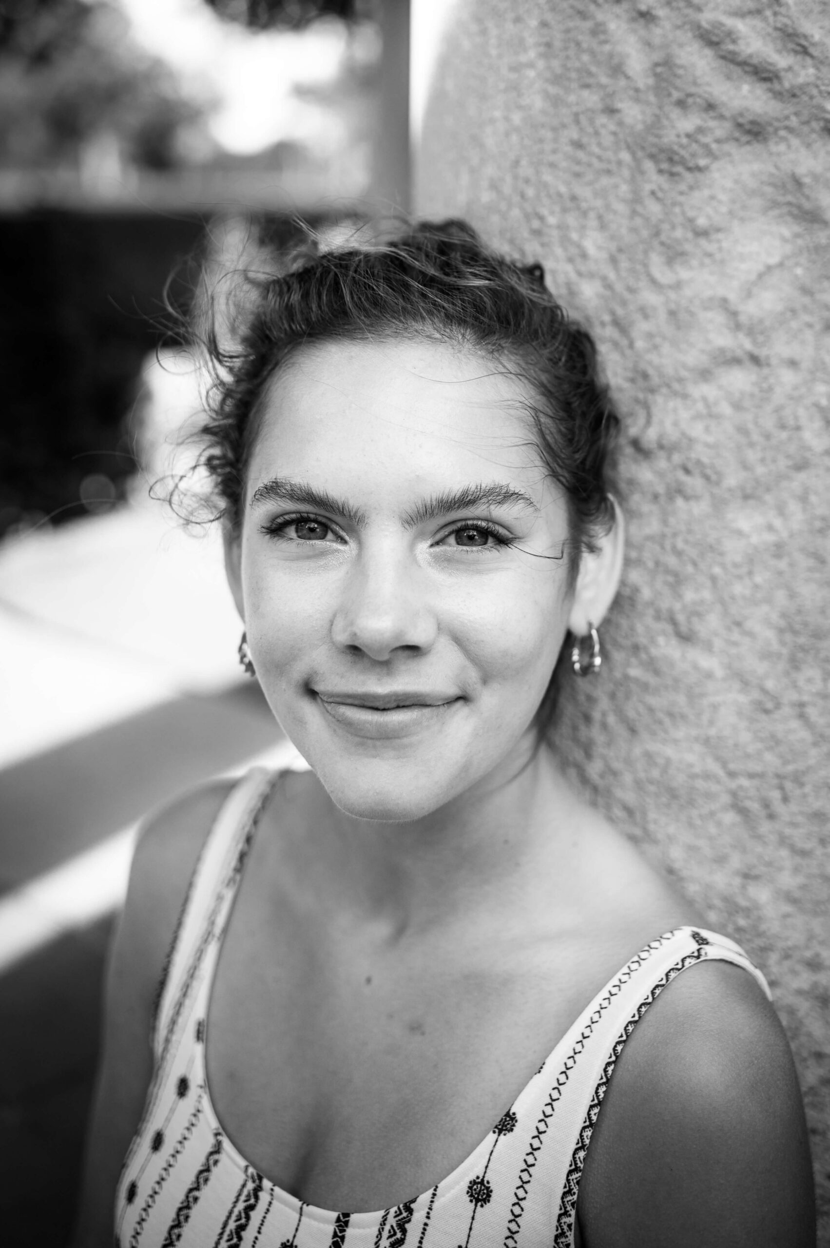 A high school senior in a pattern blouse leans against a pillar in black and white after visiting boutiques in new haven