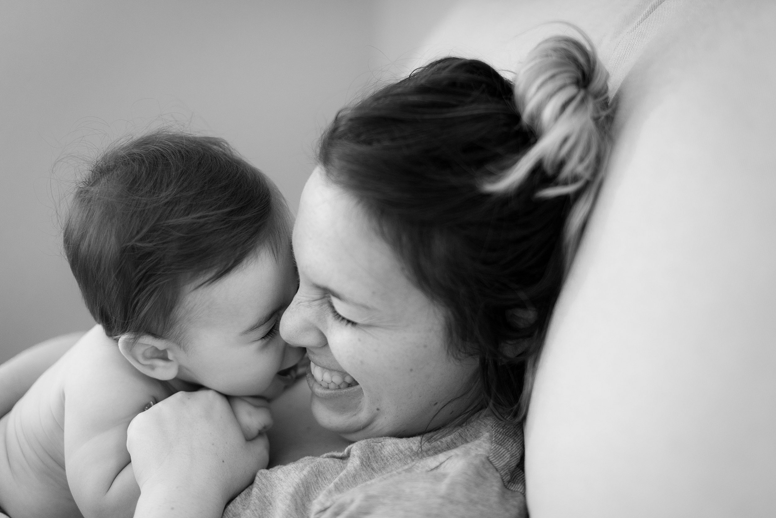 A mom giggles while laying on a couch playing with her newborn on her chest before visiting playgrounds in new haven ct