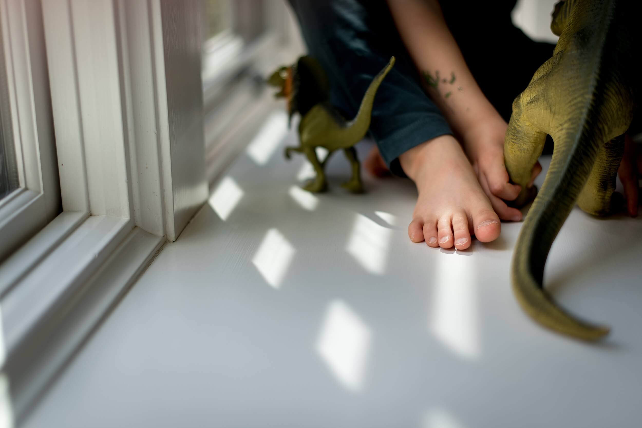 Details of a toddler's foot sitting in a window sill playing with dinosaur toys